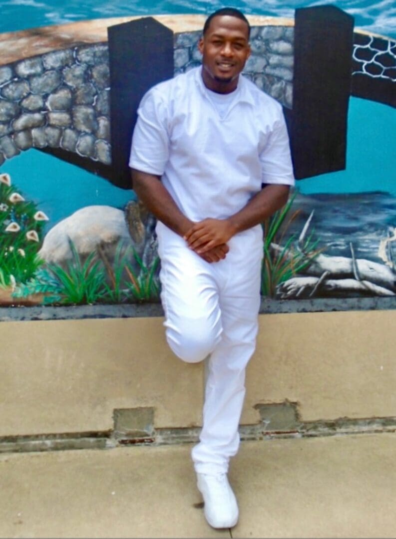Man dressed in white standing against a mural wall with aquatic animals.